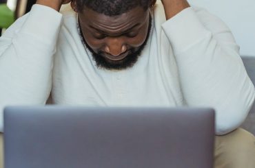 black man lowering head sitting in front of laptop