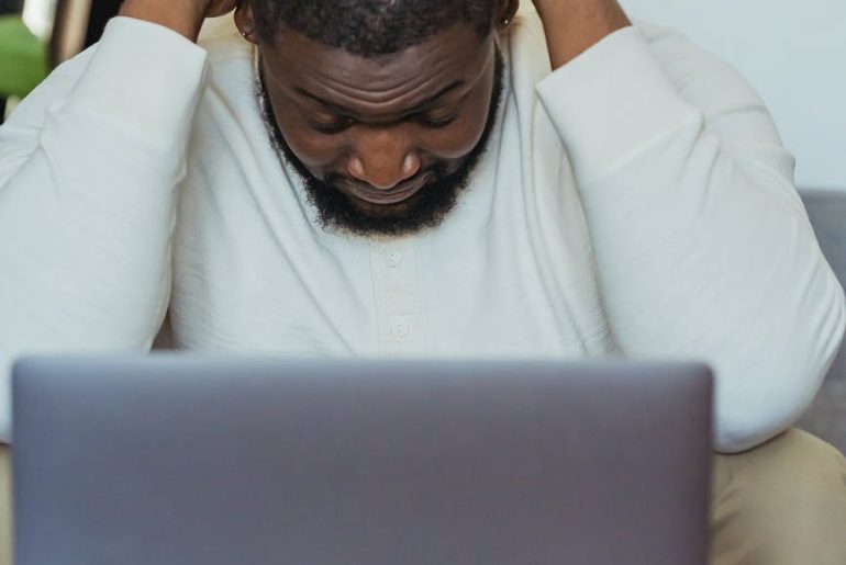 black man lowering head sitting in front of laptop
