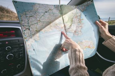 person wearing beige sweater holding map inside vehicle