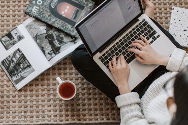 crop young businesswoman using laptop while drinking tea at home