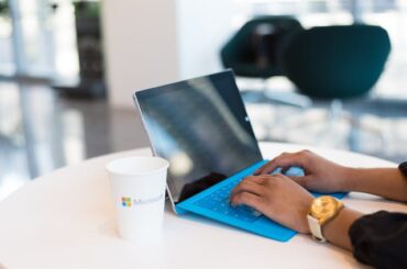 seseorang browsing di laptop dan logo microsoft di gelas